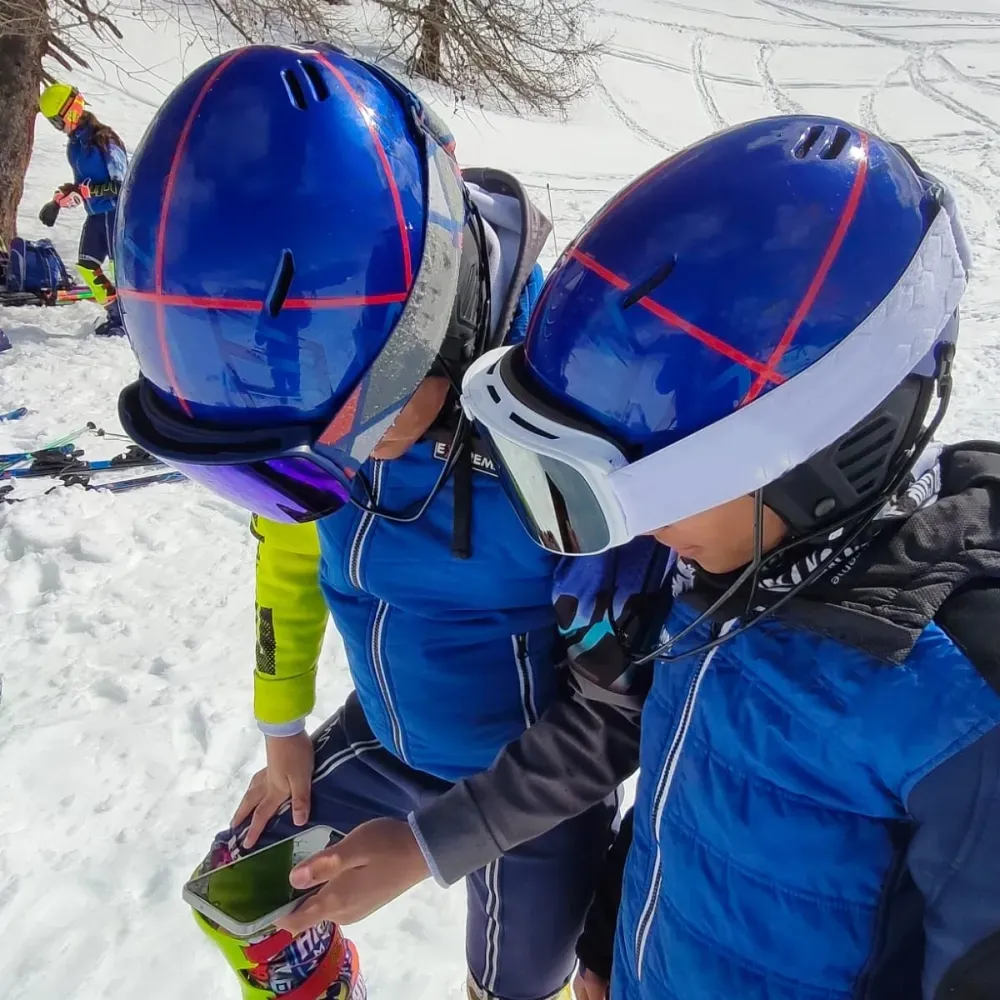 Two young skiers look at a phone together on the snow