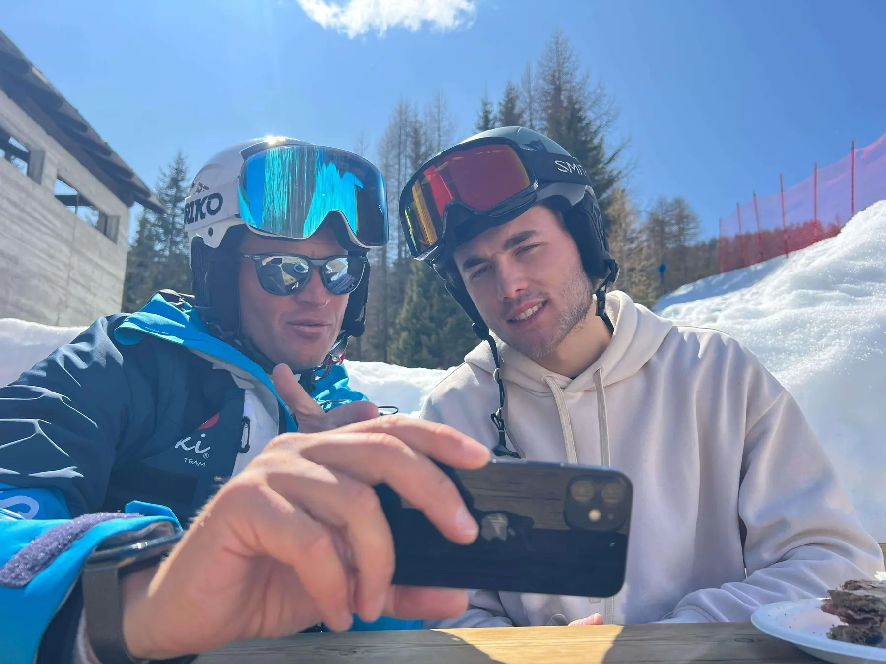 A coach and athlete review a video together on the snow